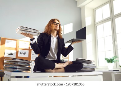 Calm Barefoot Busy Office Worker In Suit Sitting In Lotus Yoga Pose On Desk With Papers, Holding Paperwork Pile And Laptop, Breathing Deeply, Meditating And Relaxing. Balance And Stress Relief At Work