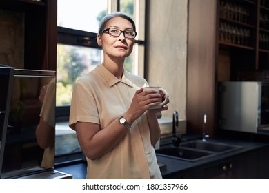 Calm Beautiful Lady Wearing Glasses Standing Alone In A Cafe Near The Sink With A Mug In Her Hands