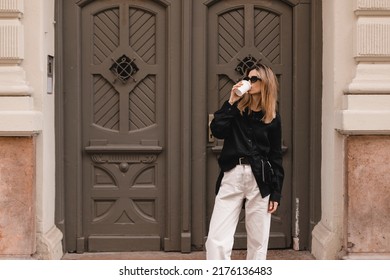 Calm Beautiful Stylish Woman Having Good Fashion Clothes Walking On Street And Holding Tea Or Coffee In Cup Takeaway With Good Mood. Girl Drink Coffee, Standing Near Wood Door And Waiting For Friends.