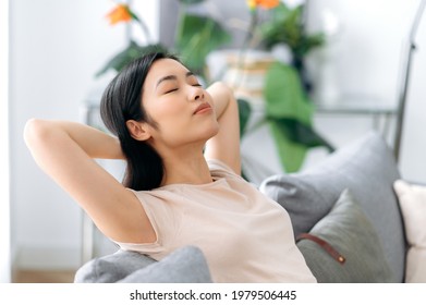 Calm Beautiful Young Asian Brunette Woman, In Casual T-shirt, Relaxing On Sofa In Living Room, Resting At Home, Dreaming About Vacation, Throwing Her Hands Behind Her Head, Closing Her Eyes, Chilling