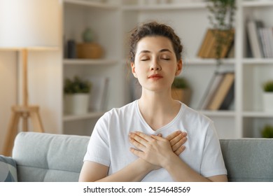 Calm beautiful young woman holding hands on her chest feeling grateful and thankful.
