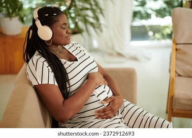 Calm Black woman closing eyes and listening to pregnancy music for mother and unborn baby - Powered by Shutterstock