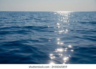 Calm blue sea shimmers with reflections of the sun creating a path of light on the waters surface