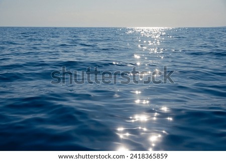 Calm blue sea shimmers with reflections of the sun creating a path of light on the waters surface