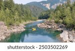 A calm blue-green river with a yellow Raft floating down it, surrounded by rocks and trees 