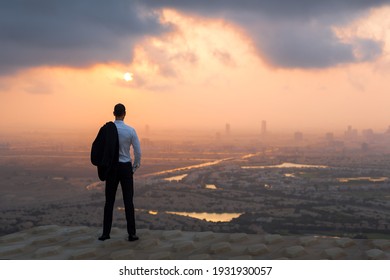 Calm business man standing above on rooftop looking at the city view at sunset. 