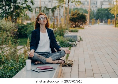 Calm business woman meditating in lotus outdoors, peaceful female freelance employee practicing yoga exercises while sitting in park after hard working day in office, holding hands in mudra
