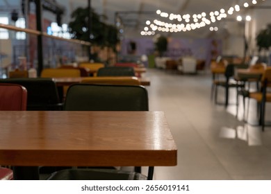 A calm cafe setting features empty wooden tables and colorful chairs in a food hall. Soft lighting creates an inviting atmosphere, offering a perfect spot for relaxation.