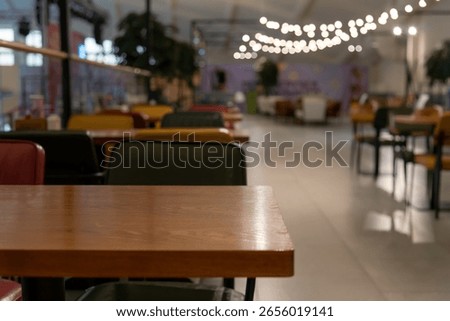 A calm cafe setting features empty wooden tables and colorful chairs in a food hall. Soft lighting creates an inviting atmosphere, offering a perfect spot for relaxation.