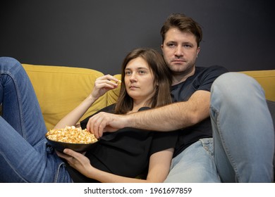 Calm, Concentrated, Unemotional Couple Hugging Lying On Couch With Popcorn In Hands And Watching TV, YouTube Channel, Online Broadcast. Evening Entertainment For Young Family Copy Space