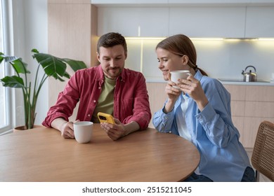 Calm content couple drink tea together, watch entertaining content on social media in morning. Scrolling videos, chatting in feeds, sharing media messages on phone, family relaxed start to day - Powered by Shutterstock