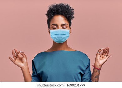Calm doctor relaxing meditation wearing respiratory mask, no stress free relief at work concept, mindful peaceful young female paramedic practicing breathing yoga exercises on beige wall. Coronavirus