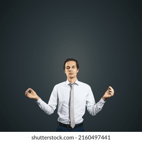 Calm Down Concept With Man In White Shirt In A Zen Pose Isolated On Dark Grey Wall Background With Empty Place For Your Text Or Logo, Mock Up