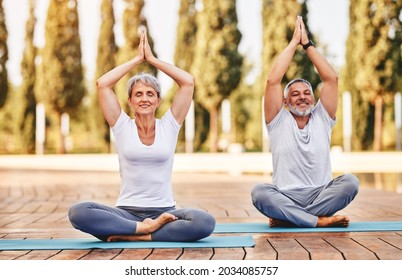 Calm Elderly Retired Family Couple Practicing Yoga Outside Happy Husband And Wife Sitting On Mats Barefoot With Eyes Closed In Lotus Position With Folded Hands Raised Up. Meditation And Mental Health