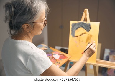 Calm elderly woman paints a portrait with paints and brush
