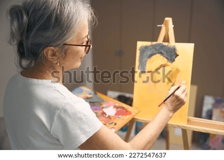 Calm elderly woman paints a portrait with paints and brush