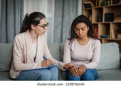 Calm European Lady Calms Sad Black Millennial Woman, Doctor Consultation Patient In Clinic Interior. Medical Support, Professional Consultation, Patient Care, Depression Therapy And Mental Problems