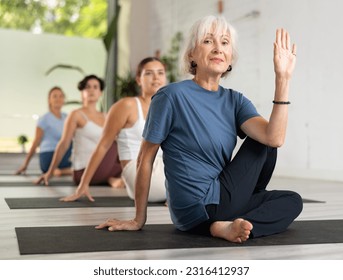 Calm European mature woman practicing Half Lord of the fishes pose or Ardha Matsyendrasana during group yoga training in fitness club - Shutterstock ID 2316412937