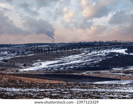 Calm evening sunset in the Ukrainian countryside. Arable land covered with the last snow, early spring Industrial chimneys of Burshtyn TPP on the horizon.