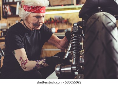 Calm female retiree repairing wheel of motorcycle