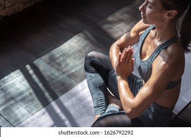 Calm fit sporty healthy mindful woman sit in lotus pose doing yoga exercise breathing fresh air meditating in studio lit with sunlight, stress free peace of mind concept, copy space, close up view