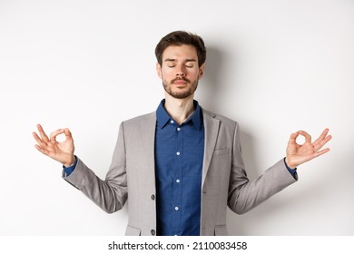 Calm and focused businessman meditating with eyes closed and hands spread sideways, finding peace in meditation, practice yoga breathing, standing on white background - Powered by Shutterstock