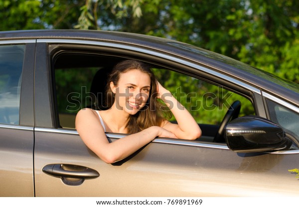 Calm girl with a smile with long dark hair\
looks out the window of a brown\
car