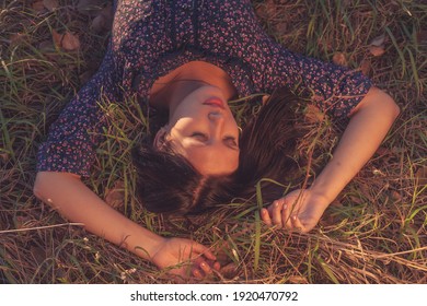 Calm girl in vintage clothes lying on brown grass. Fashionable lady wearing a ornate print is having relax with on the lawn. Leisure in rural area.