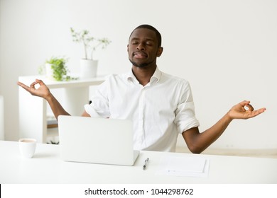 Calm happy african american man meditating at home office desk with laptop developing focus and concentration, black employee practicing yoga at work, no stress free, positive thinking, peace of mind