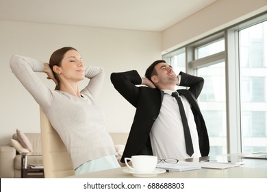 Calm happy businessman and businesswoman relaxing with eyes closed, hands behind head sitting in ergonomic office chairs, smiling executives enjoying break, lounge after work in modern office - Powered by Shutterstock