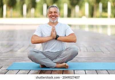 Calm happy mature  man sitting in lotus pose on mat during morning meditation in park, holding hands in namaste gesture and smiling at camera,  male meditating. Mental health and yoga concept - Powered by Shutterstock