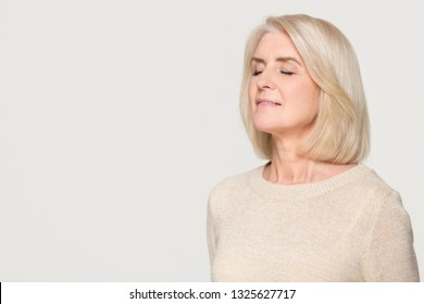 Calm Happy Mature Mid Aged Woman Inhaling Taking Deep Breath Of Fresh Air Feel No Stress, Mindful Old Lady Meditating Relaxing Advertise Freshener Isolated On White Grey Studio Background, Copy Space