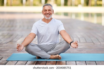 Calm happy senior man sitting in lotus pose on mat during morning meditation in park, holding hands in mudra gesture and smiling at camera. Mental health and yoga concept - Powered by Shutterstock