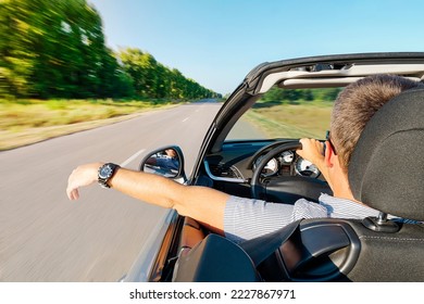 calm happy successful man sit in the car hand is driving the car on the road. young guy inside an expensive convertible is driving on a road outside city against backdrop of beautiful summer nature.