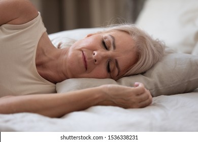 Calm Healthy Mature Older Woman Lying On Comfortable Pillow Orthopedic Mattress Sleeping Well In Cozy Bed, Serene Middle Aged Lady Beautiful Face Enjoy Peaceful Sleep Relax At Home, Close Up View