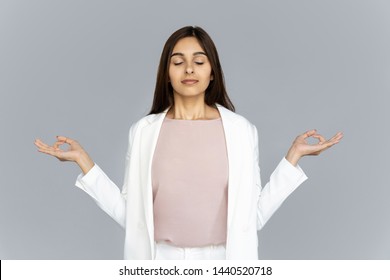 Calm Healthy Mindful Indian Business Woman Wear Suit Meditating Doing Yoga Exercise With Eyes Closed Breathing Fresh Air Relaxing Feel Zen No Stress Free Relief Isolated On Grey Studio Background