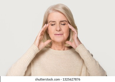Calm healthy old mature woman touching head massaging temples feeling stress relief, relaxed mindful middle aged woman meditating relieving headache isolated on white grey studio background