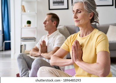 Calm healthy serene old middle aged senior 50s couple meditating with eyes closed namaste hands at home together. Senior retired man and woman doing yoga exercise, breathing, feeling no stress, zen. - Powered by Shutterstock