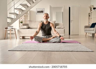 Calm healthy serene old middle aged senior tattooed man meditating with eyes closed sitting in yoga pose in living room at home. Breathing exercises, meditation, no stress, peace of mind, zen concept. - Powered by Shutterstock