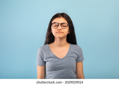Calm Indian Teen Girl Posing With Closed Eyes, Meditating Or Praying To God Over Blue Studio Background. Peaceful Teenager In Glasses Practicing Yoga For Stress Relief And Inner Harmony