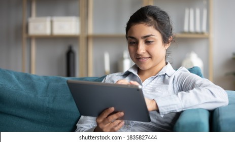 Calm Indian Woman Resting On Couch At Home Hold Tablet Modern Device Smile Read Message Enjoy Remote Shopping Online, Distance Chat With Friend, Plan Vacation Booking Hotel And Travel Buy Tour Concept