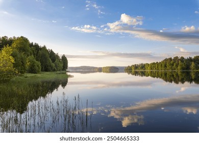 A calm lake with a cloudy sky in the background. The sky is blue and the trees are green - Powered by Shutterstock