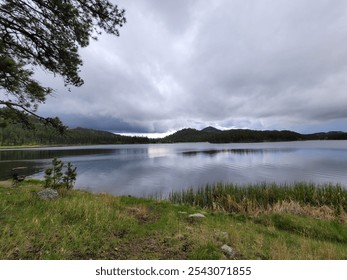 Calm lake with dramatic sky reflected in the lake with mountains in the background. Cloudy sky over dark hills with green grass in the foreground. - Powered by Shutterstock