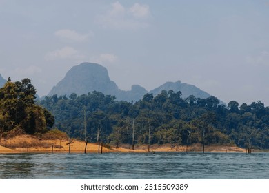 A calm lake reflects the surrounding landscape, featuring vibrant greenery and a distant mountain range under clear skies, creating a peaceful and scenic atmosphere. - Powered by Shutterstock