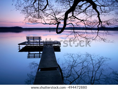 Calm Lake at Sunset, Wooden Pier with Bench under a Bare Tree