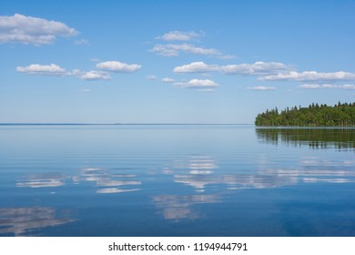 Calm lake surface with the clouds reflected in it and a piece of forest in a good weather 