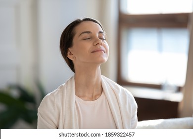 Calm Leisure. Content Young Woman Spending Time At Home Alone, Sitting On Sofa With Eyes Closed In Delight, Breathing Fresh Cool Air Because Of Working Conditioner, Giving Face To Sunlight From Window