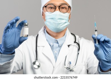 Calm Mature Chinese Male Doctor In White Coat, Protective Gloves, Mask And Glasses Show Vaccine And Syringe, Isolated On Blue Background, Studio. Immunization, Health Care, Medicine And Treatment