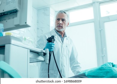 Calm mature medical worker standing with an endoscope and looking at the screen stock photo