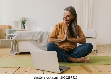 Calm Middle-aged Woman Holding Hands In Namaste Gesture. Mature Yoga Teacher Practicing Meditation Online At Home. Zen, Balance And Self-awareness Concept